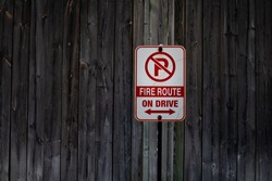 A vertical and rectangle shaped no parking sign signifying a fire route is tacked up to a weathered wooden fence in London, Ontario, Canada, February 2021.  