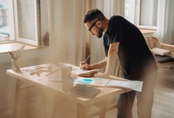 A young artist makes a sketch with a brush in the workshop. A creative person is standing over a desktop with a brush in his hand. Creative studio, lifestyle, the process of creating a work of art.