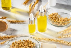A conceptual composition of wheat essential oils, a bath brush and wheat germ on a marble table. Wheat serum oil for skin and hair care. Bottle of body oil with a dropper. Self-care, spa and wellness.
