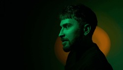 Side view artistic creative portrait of man looking away in orange neon lights on dark green background. Modern photo handsome bearded middle age man with earringsin the ear. Copy space. Banner