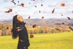 Young Asian Woman Throwing Autumn Leaves in The Air With Fall Foliage and Vermont’s Green Mountains in The Background