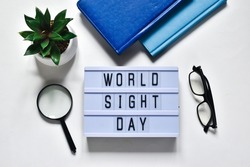Glasses that correct eyesight, magnifying glass, notepads, green plant and light box with text WOLD SIGHT DAY on a white background. Flat lay. Holiday concept.