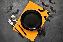 Halloween table setting. Empty plate with cutlery and blank orange card with spider, bats on gray background. Flat lay, top view trendy holiday concept. 