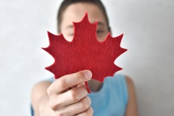 The boy hold red maple leaf made of paper covering his face on a light background. Canada day. Copy space. Selective focus