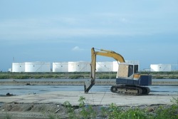 The backhoe stopped after the excavation work was completed. Behind it is a large white industrial tank for water and oil.