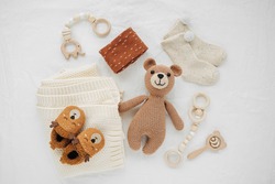 Knitted toy bear, blanket, socks,  and wooden teether for newborn on white bed.  Gender neutral  baby stuff and accessories. Flat lay, top view