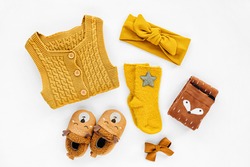 Yellow knitted romper, hairband, socks and cute baby slippers.  Set of newborn clothes and accessories. Flat lay, top view 