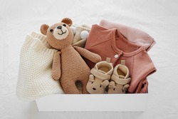 Box with baby stuff and accessories for newborn on bed. Gift box with knitted blanket, clothes, socks, shoes and toy. Baby shower concept.  Flat lay, top view