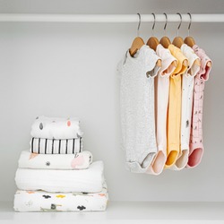 Set of baby bodysuits for a newborn girl and boy on hangers in white wardrobe. Motherhood, cleaning home kids wardrobe. Minimal fashion concept.