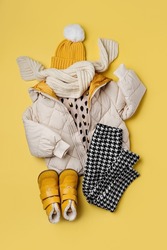 Kids warm puffer jacket with hat and boots on yellow  background. Stylish childrens outerwear. Winter fashion outfit 