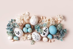 Easter eggs with sweets and flowers on beige. Happy Easter concept. White and blue eggs and cute nest with candy 