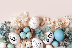 Easter eggs with sweets and flowers on beige. Happy Easter concept. White and blue eggs and cute nest with candy 