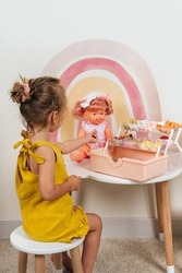 A little girl plays with doll and hair accessories in Children's room. Girl doing hair to a doll with bows. Educational game for baby and toddler in modern nursery. 