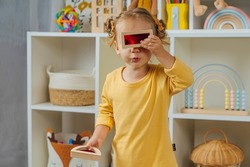Toddler  looking through the colorful window of a toy. Educational game for baby  in modern nursery. A little girl looking through transparent colored block toy. Wooden rainbow stacking blocks. 