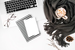 Workspace with laptop, notebook with empty card, coffee cup wrapped in scarf,  glasses. Stylish office desk. Autumn or Winter concept.  Flat lay, top view