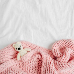 A small knitted baby toy-bear is covered with a warm blanket, flat lay,  top view