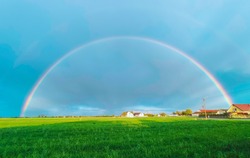 Summer rainbow landscape. Houses and field in the countryside in the background.