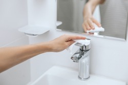 Cleaning the sink faucet with a microfiber cloth. Sanitize surfaces prevention in hospital and public spaces against corona virus. Woman hand using wet wipe. Cleaning the bathroom.