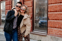 Couple of happy people hugging in the city. A man and a woman of European appearance in sunglasses on the street in outerwear.