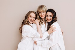 three beautiful women of European appearance hug and smile on a pink background. Several ladies in white shirts. Female friendship. High quality photo