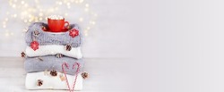 A stack of knitted sweaters or scarves, a cup of cocoa with marshmallows, christmas decorations on a blurry bokeh background. Winter holidays concept, cozy home atmosphere. Banner. Copy space.