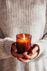 Woman in cozy sweater holding burning candle close-up. Cozy autumn or winter, hygge lifestyle