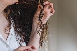Close-up of feminine hand holding a strand of her wavy hair. Styling with curly method