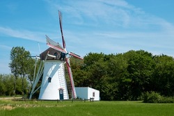 Dutch beautiful windmill on green meadow and tall trees, with outbuildings. Netherlands
