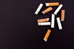 Lots of dirty used cigarette butts on a black background. Health, smoking, harm to health, Cancer of the lungs. View from above. Copy space for text. Located on the right