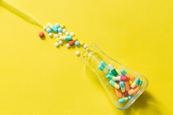 pills and pill bottles on yellow background,Brown medical glass drug bottle and some pills around with a cap on yellow,Erlenmeyer Flask. Empty Glass Conical Lab Container
