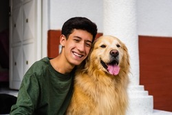 latin teenager laughing and hugging his golden retriever dog sitting in the driveway