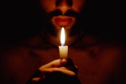 shirtless young man holds a candle in his hands, opening the third eye with fire