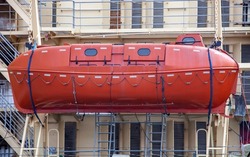 An orange closed-type Arctic lifeboat on board an icebreaker.  Rescue weltbot on the background of the superstructure and the rails of marine vessel.  