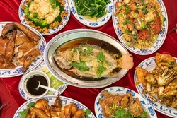 Flatlay of a full table spread containing traditional dishes for Chinese Lunar New Year. Each dish has a symbolic meaning for the celebration.