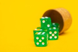 Green dice with a value of five fell out of the dice container on a yellow background: a place for text, a concept of table board games for the whole family, a casino game