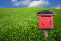 A red wooden postbox lay on the green grass and blurred sky.