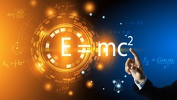The scientist's hand points to the equation of relativity of Albert Einstein. E equals m multiplied by c squared. In the concept of a physics equation ring and a dark blue background.