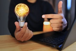 A person holding a light bulb and a brain-shaped light line represents creativity and new ideas in work.