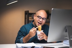 Young asian business freelancer working at late night. He very hungry and eating hot instant noodle and work with computer in the dark office at night.