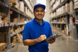 Young worker in blue uniform checklist manage parcel box product in warehouse. Asian man employee holding clipboard working at store industry. Logistic import export concept.