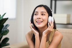 Relaxing time with music. Beautiful young asian woman sitting in the house choose music and take a rest and listening song with wireless headphone. Lifestyle in living room at house in the morning.