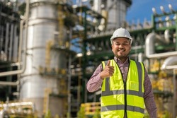 Asian engineer man with white safety helmet standing front of oil refinery. Industry zone gas petrochemical. Factory oil storage tank and pipeline. Workers work in the refinery construction building