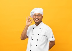 Happy Young handsome asian man chef in uniform with hat standing posting okay taste delight delicious hand gesture. Cooking indian man Occupation chef or baker People in kitchen restaurant and hotel.