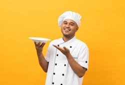 Attractive Young handsome asian man chef in uniform holding empty plate delicious dish menu good taste on isolated. Cooking indian man Occupation chef or baker People in kitchen restaurant and hotel.