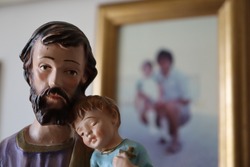 Father's day concept. Statuette of Saint Joseph with sleeping Baby Jesus and a picture of Father and Daughter on the Background