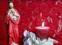Home altar to the Sacred Heart of Jesus Christ prepared for the month of June. Statuette with candle light and white flowers