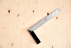 Steel framing set square on a wooden background. L-square instrument. Right angle. Silver color. Copy space. Plywood backdrop. Building rule. Measurement tool. Carpentry device. Triangle 90 degrees.