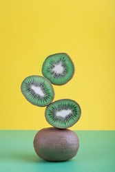Balancing group of ripe juicy kiwi fruit slices against colorful yellow and green background representing balanced diet and healthy eating. Vertical orientation image. Modern color concept