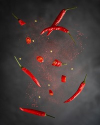 Levitation or flying of red chili pepper whole and slices with paprika powder used for food seasoning to make hot spicy flavour in mexican and asian cuisine against dark black background. Vertical