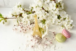 Eiffel tower figurine, macarons and branches with white cherry blossoms on a white background. Spring still life, travel France.